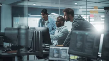 Tres personas trabajando en computadoras en una oficina moderna.