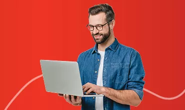 Hombre con gafas sonriendo, de pie, sosteniendo un portátil en alto. Parece feliz y entusiasmado.